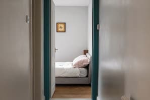 A narrow hallway leading to a bedroom with a bed, a single wall-mounted picture, and a door with teal trim. - 40 Grimsey Road, Leiston (Suffolk)