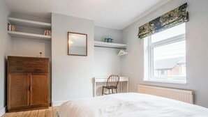 Et soveværelse med en seng, et træskab, et skrivebord, en stol, en radiator, et vindue og et spejl.