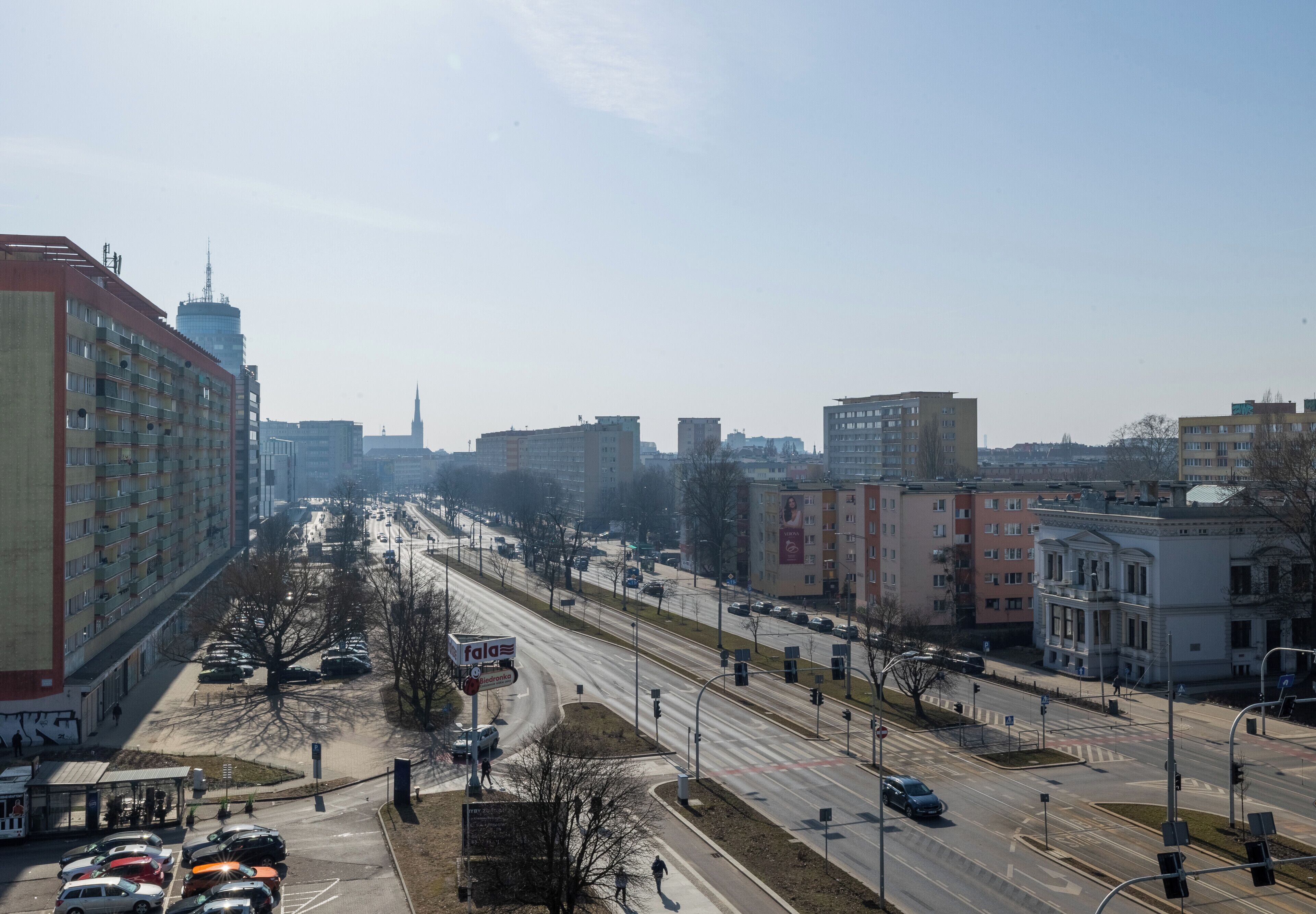 A cityscape with a prominent building on the left, a clear sky, and a busy road with vehicles.