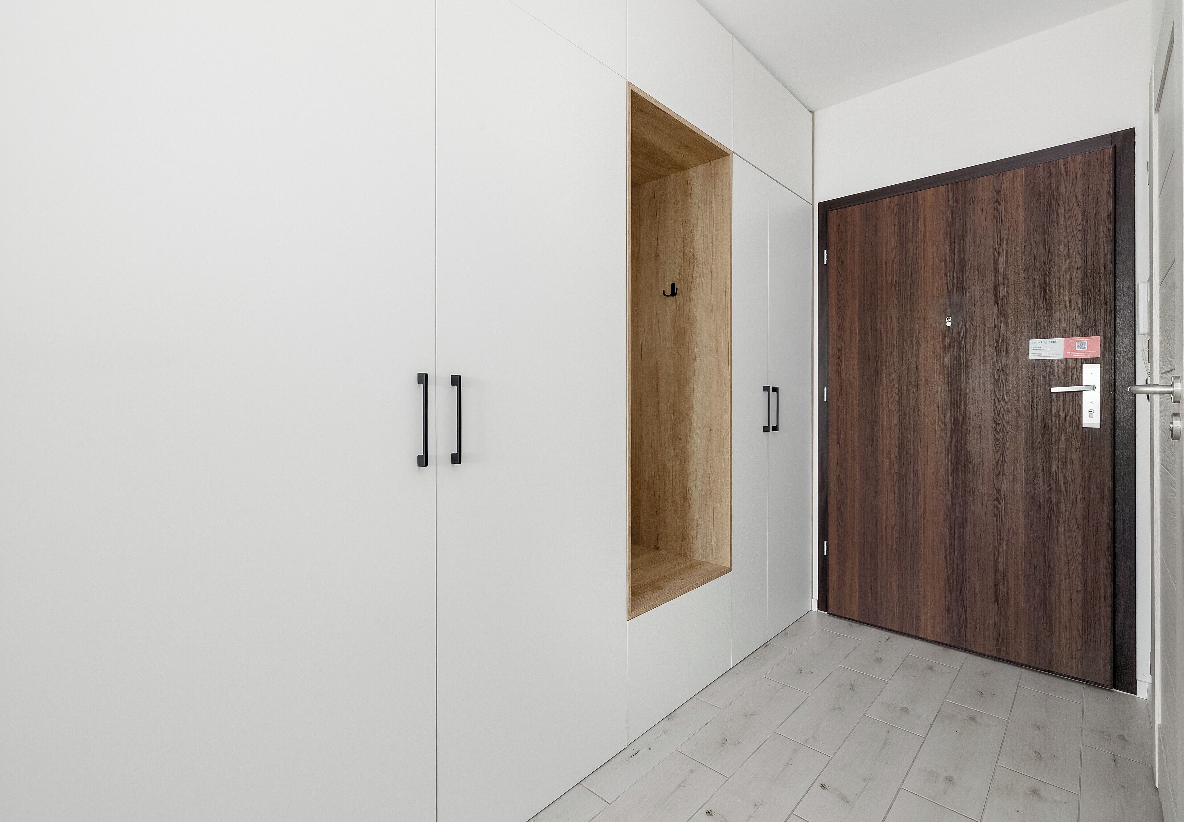 Un pasillo con paredes blancas, una puerta de madera y un armario blanco con tiradores negros.