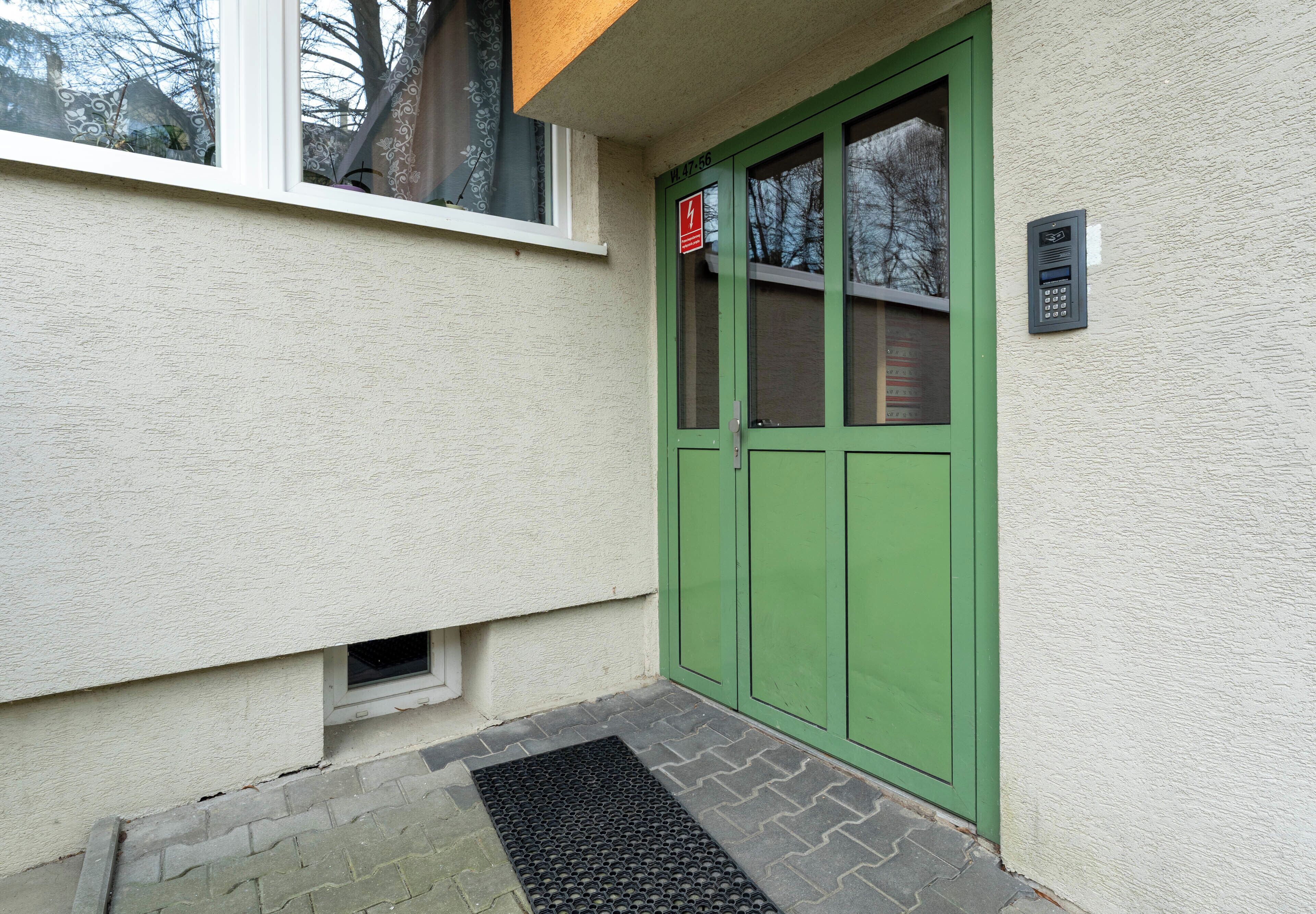 Eine grüne Tür mit Zahlenschloss, einem kleinen Fenster und einem Klingel.