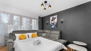 Una camera da letto moderna con un divano grigio, un letto bianco, un tavolino rotondo e un'ampia finestra con tende.