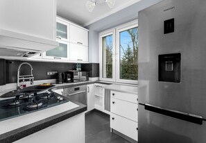 A modern kitchen with stainless steel appliances, a water dispenser, and a window with a view of trees.