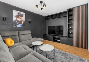A modern living room with a grey sofa, two white round tables, a TV, and a wooden floor.