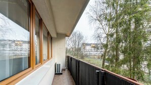 Un balcone con ampie finestre, pavimento piastrellato e vista su alberi e edifici.
