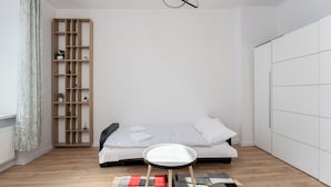 A minimalist bedroom with a single bed, a small stool, a wooden shelving unit, and a wardrobe. - Daszyńskiego Urban Comfort Apartment (Gliwice)