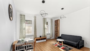 A modern living room with a wooden dining table, chairs, a black sofa, a bookshelf, and a clock on the wall. - Daszyńskiego Urban Comfort Apartment (Gliwice)