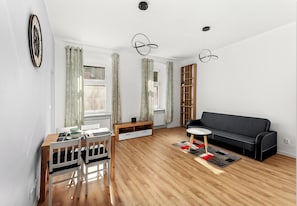 Un salon moderne avec une table à manger en bois, des chaises, un canapé noir, une bibliothèque et une horloge au mur.
