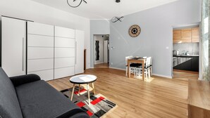 A modern living room with a sofa, a dining table, and a kitchen in the background. - Daszyńskiego Urban Comfort Apartment (Gliwice)