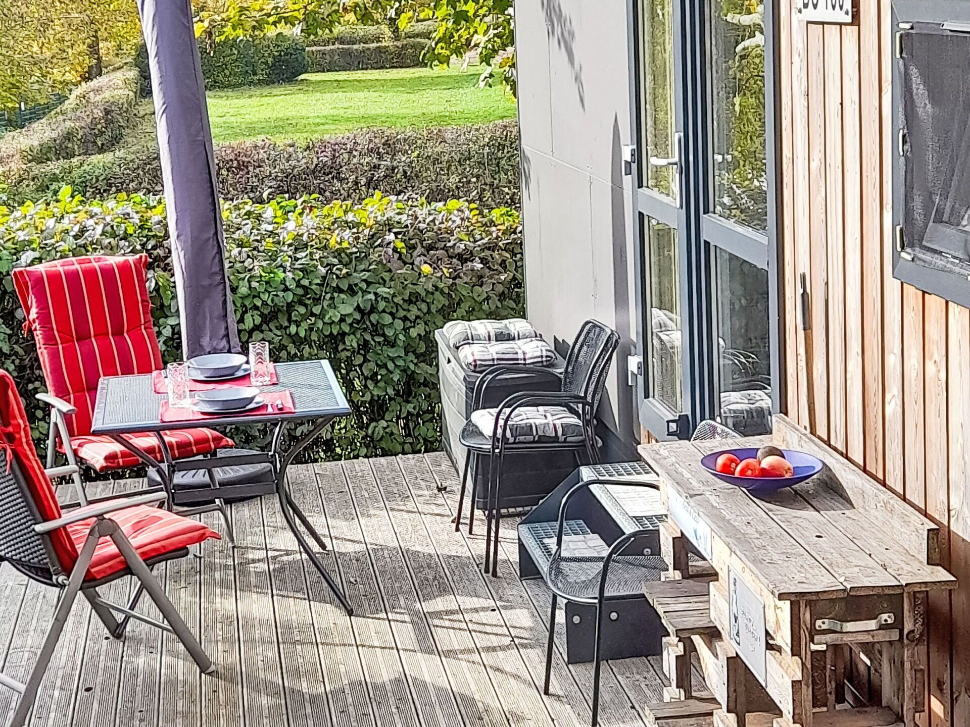 Un patio al aire libre con una mesa y sillas de madera, un vidrio que da a un jardín y vistas a un césped bien cuidado.
