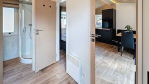 Ein modernes Interieur mit Holzboden, einer Glasdusche, einer Küchenzeile mit Mikrowelle und einem Essbereich mit einem Stuhl und einer Pflanze.