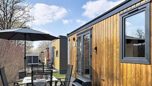 Ein modernes Holzhaus mit großen Fenstern, einer Terrasse mit Gartenmöbeln und einer überdachten Patio.