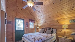 Een gezellig houten slaapkamer met een bed, nachtkastjes, een plafondventilator en een raam met jaloezieën.