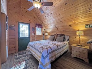A cozy wooden cabin bedroom with a bed, nightstands, a ceiling fan, and a window with blinds. - Hideaway Cabin Bryson City, NC - 5 Minutes from Downtown (Bryson City)