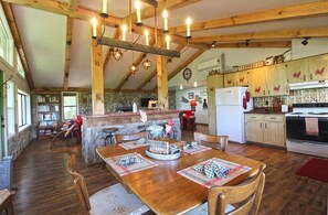 A rustic farmhouse interior with a wooden dining table, a kitchen with wooden cabinets, and a stone fireplace. - View 280- Amazing views of the Smoky Mountains (Bryson City)