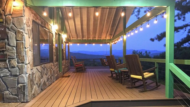 A wooden deck with chairs, a stone wall, and a view of mountains. - View 280- Amazing views of the Smoky Mountains (Bryson City)