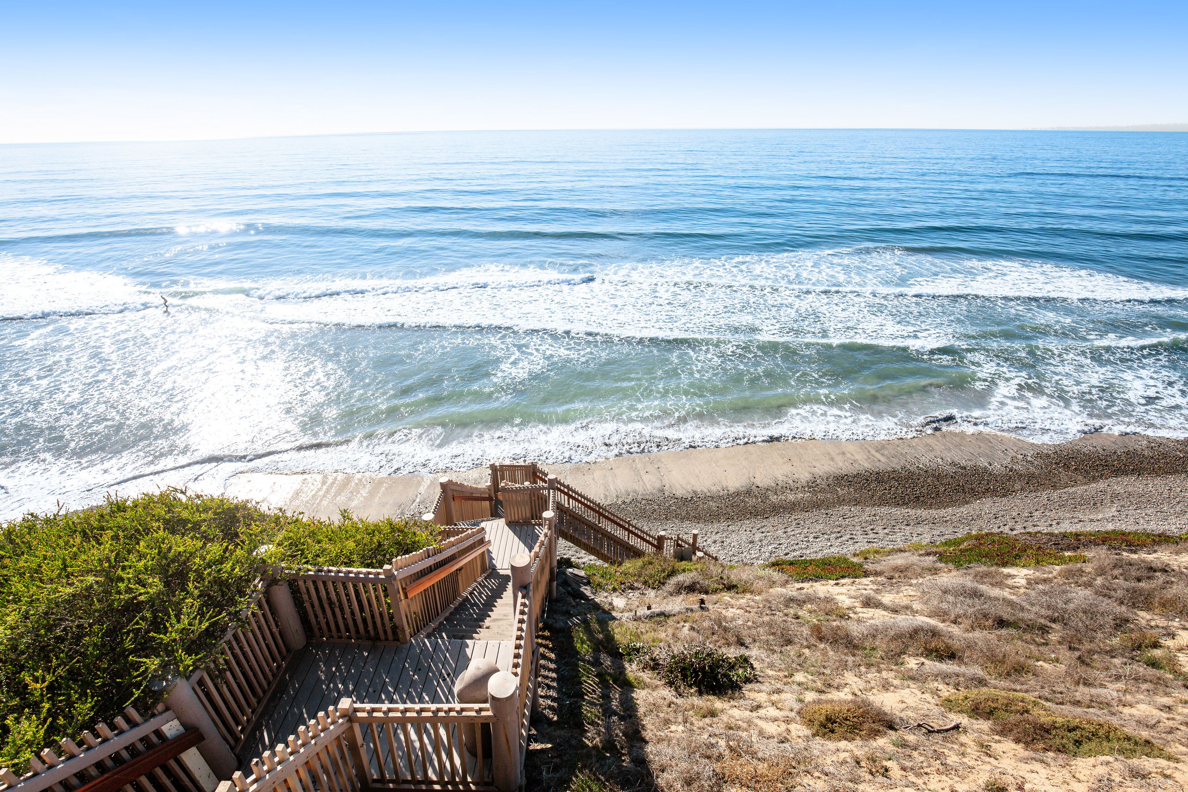 Une promenade en bois mène à une plage où les vagues viennent se briser sur le rivage.