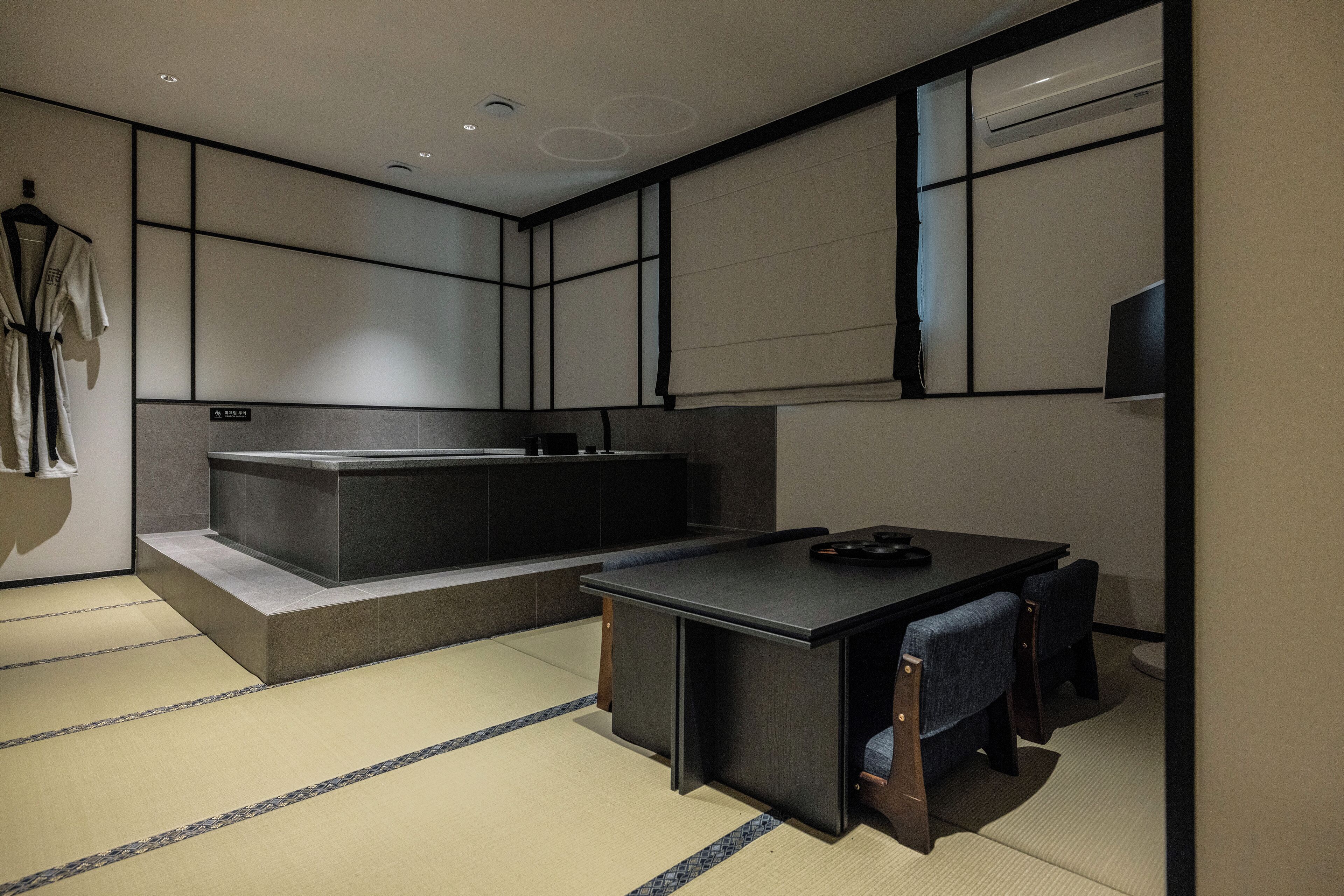 Une chambre moderne avec un sol recouvert de tatamis, un bureau noir et une grande baignoire.