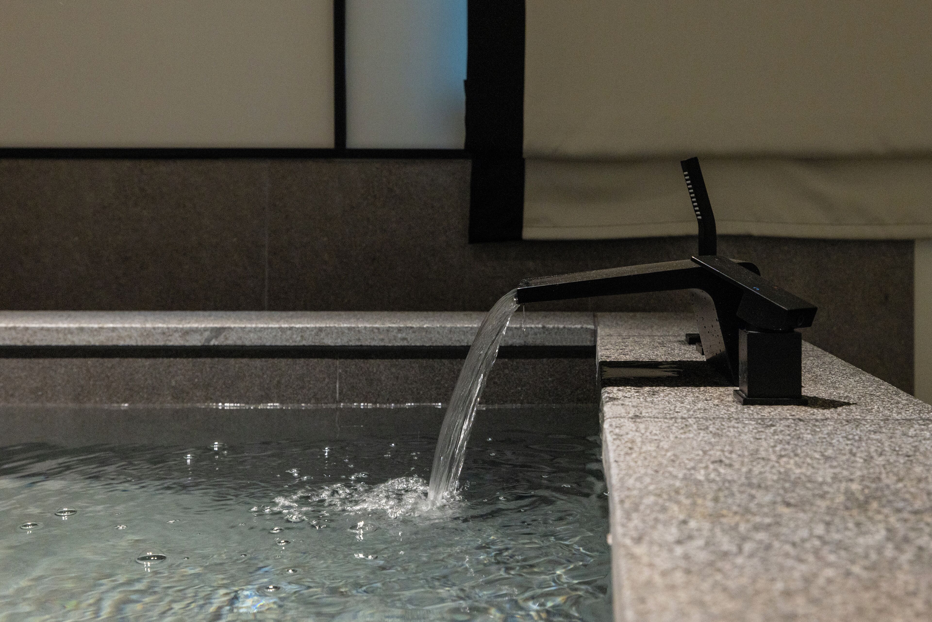 A water feature with a spout and a black stand, set against a tiled wall.
