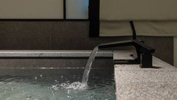 A water feature with a spout and a black stand, set against a tiled wall.