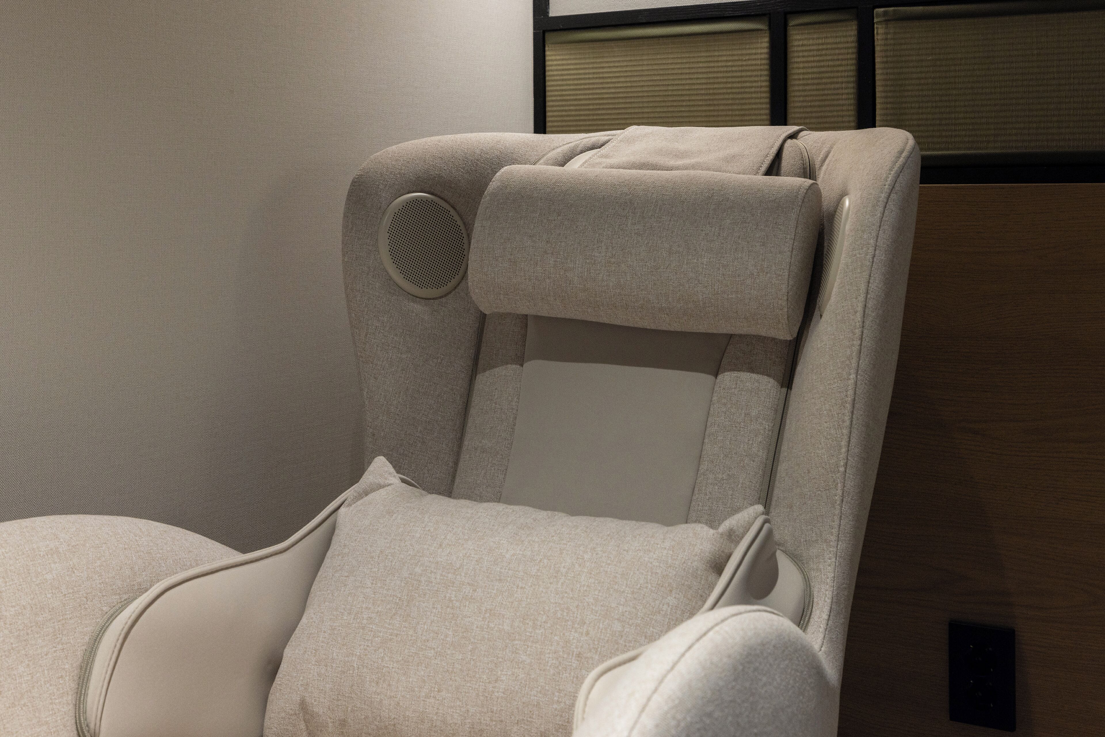 A reclining chair with a headrest and side support, a control panel, and a wooden panel wall.