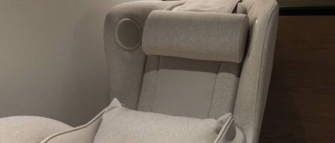 A reclining chair with a headrest and side support, a control panel, and a wooden panel wall.