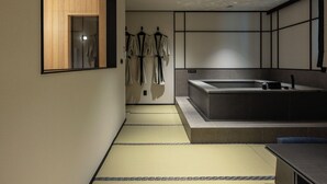 A modern bathroom with a large bathtub, a wooden window, and a towel rack with robes. - mitasuyaryokanhotel by anook gangneung (Gangneung)