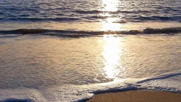 Une plage avec des vagues et la lumière du soleil se reflétant sur l’eau.