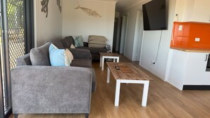 A modern living room with a grey sofa, a wooden coffee table, and a TV mounted on the wall. - 3 Bedroom, 2 Bathroom Holiday House (Karumba)