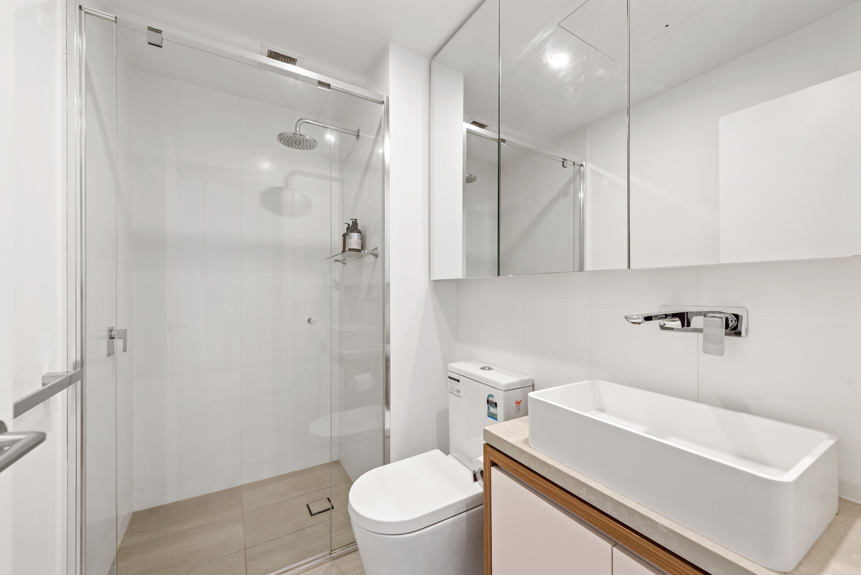 Un bany modern amb un armari de dutxa de vidre, un lavabo blanc i un vàter.