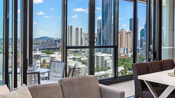 A modern hotel room with large floor-to-ceiling windows, a dining area, and a view of a cityscape. - Skyline Apartment in Fortitude Valley (Fortitude Valley)