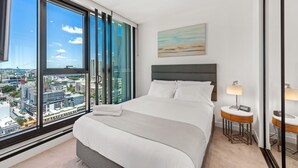 A hotel room with a large window, a bed, a bedside table with a lamp, and a painting on the wall. - Skyline Apartment in Fortitude Valley (Fortitude Valley)