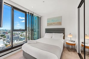A hotel room with a large window, a bed, a bedside table with a lamp, and a painting on the wall. - Skyline Apartment in Fortitude Valley (Fortitude Valley)