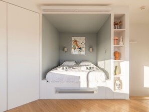 A modern bedroom with a bed, bedside lamps, a painting, and a shelf with decorative items. - Panoramic duplex in Biarritz, sea and lighthouse view (Biarritz)