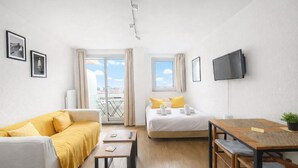 Habitación de hotel con cama, sofá, mesa de comedor, televisor y balcón con vistas.