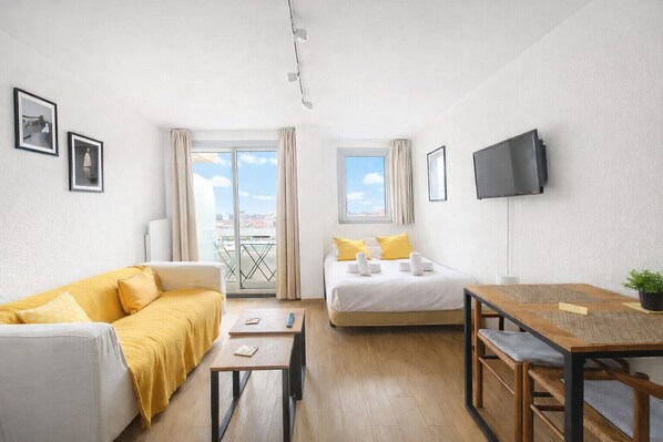 Une chambre d’hôtel avec un lit, un canapé, une table à manger, une télévision et un balcon avec vue.