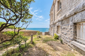 A stone building with a view of the sea, a paved path, and some greenery. - Beachfront Apartment with Terrace, Biarritz (Biarritz)