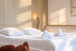 A hotel room with a bed, pillows, a wall-mounted light, and a towel on the bed. - Beachfront Apartment with Terrace, Biarritz (Biarritz)