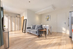 A modern living room with a grey sofa, wooden flooring, a dining table with chairs, and a large mirror. - Beachfront Apartment with Terrace, Biarritz (Biarritz)