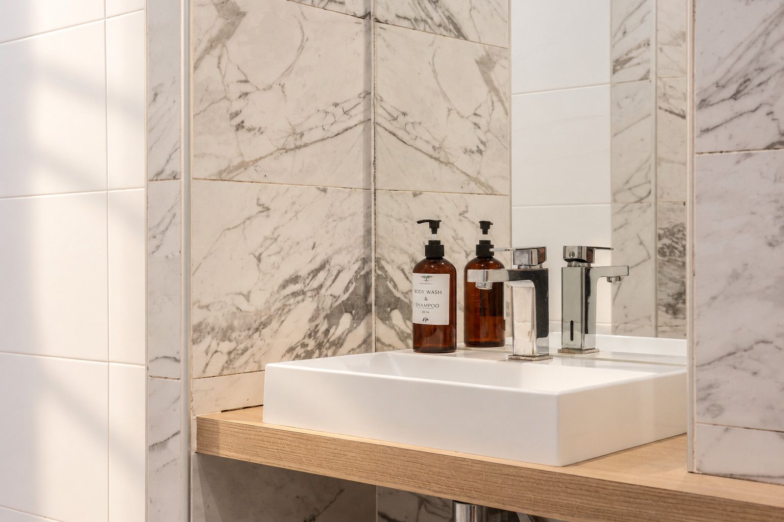 Ein Badezimmer mit einem weißen Marmorwaschbecken, zwei Flaschen Duschgel und Shampoo sowie einem Chromarmaturen-Set.