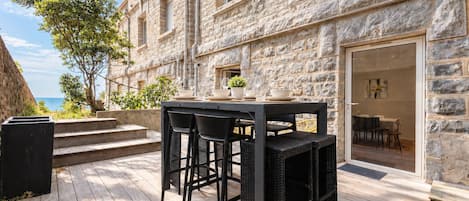 A stone building with a wooden deck, outdoor seating, and a view of the sea.