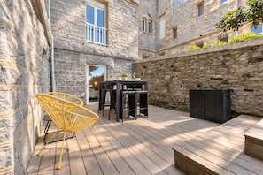 Ein Steinhaus mit einer Holzterrasse, Sitzgelegenheiten im Freien und einer Tür zu einer Glastür.