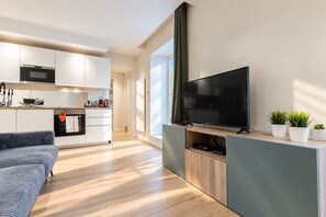 A modern kitchen with white cabinets, a flat-screen TV, and a wooden dining table. - Beachfront Apartment with Terrace, Biarritz (Biarritz)