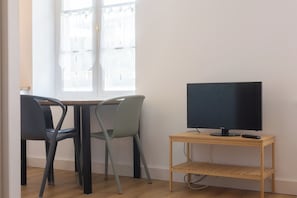 Una habitación con un escritorio de madera, dos sillas, un televisor y una ventana con cortinas.