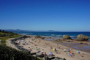 Una playa con gente, sombrillas y rocas grandes.