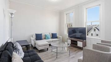 Un salon comprenant un canapé, une table basse, un téléviseur et une fenêtre donnant sur une maison.