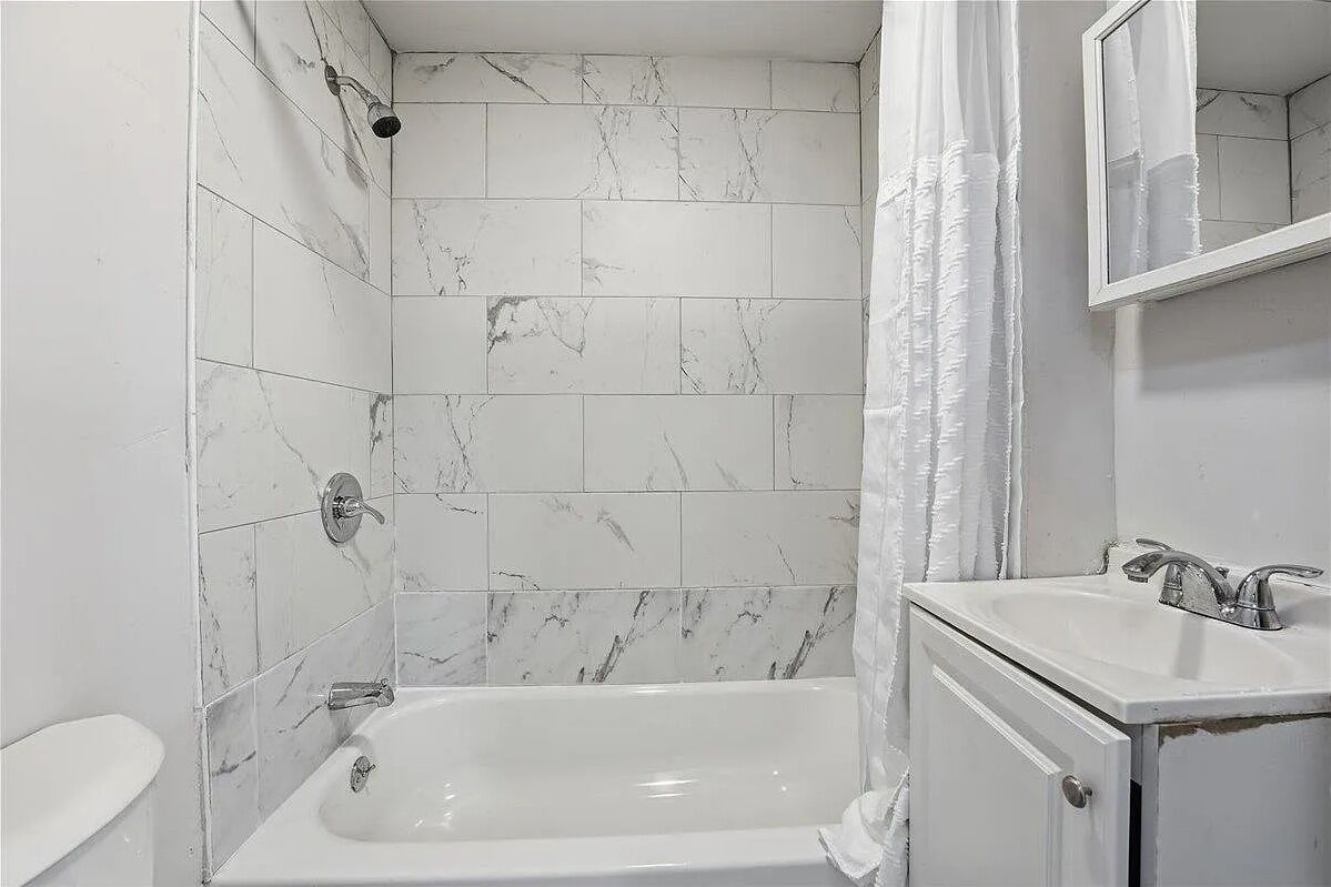 Une salle de bain avec des carreaux de marbre blanc, une baignoire, un lavabo et un miroir.