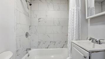 Une salle de bain avec des carreaux de marbre blanc, une baignoire, un lavabo et un miroir.