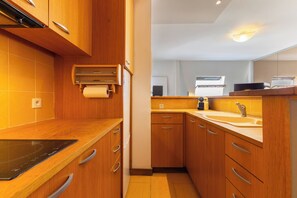 Une cuisine compacte dotée de meubles en bois, d’une plaque de cuisson à induction noire, d’un évier et d’un four encastré.