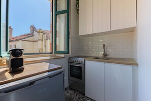 A compact kitchen with a built-in oven, a stovetop, a sink, and a window with a view of neighboring buildings. - Cozy Apartment in the Heart of Biarritz (Biarritz)